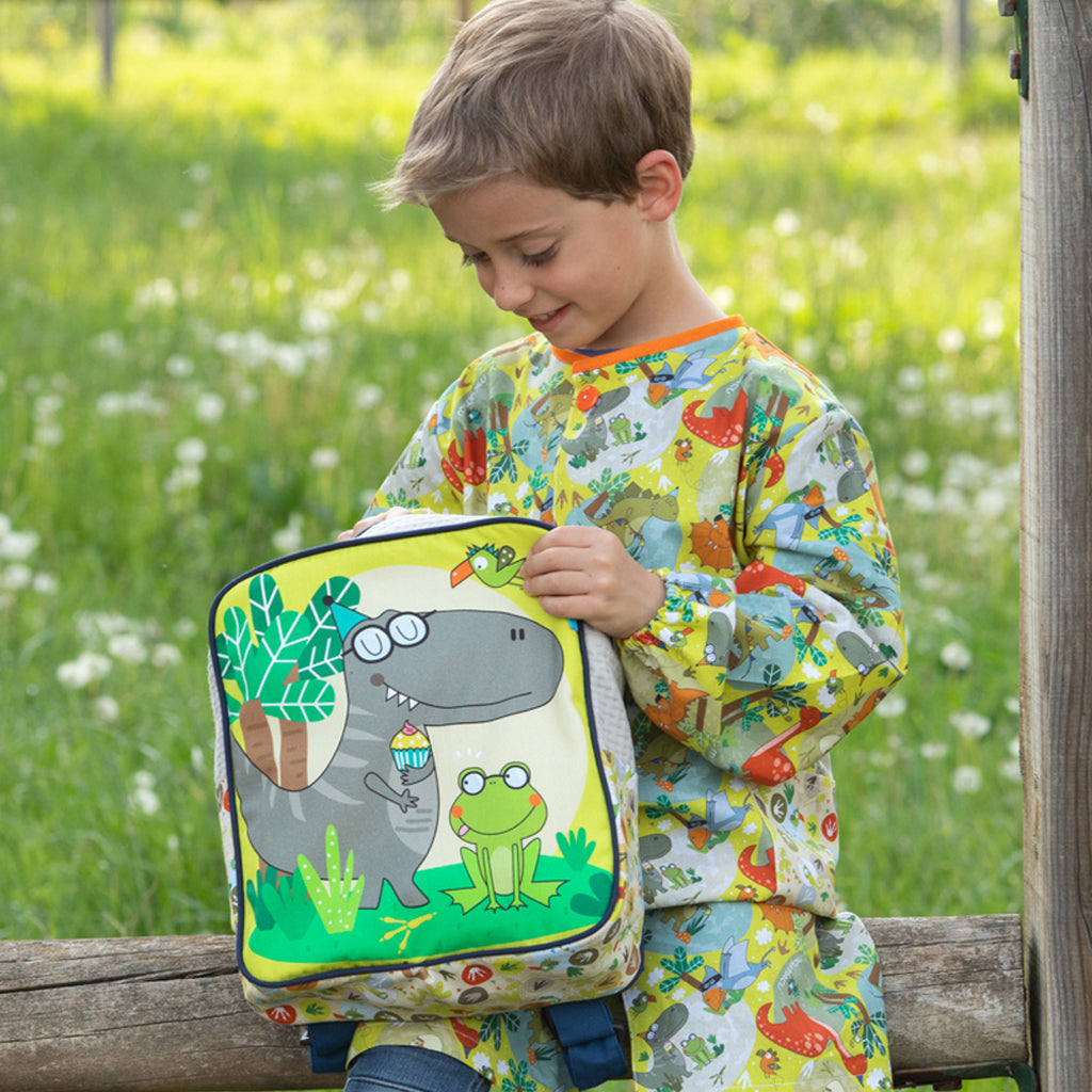 Foto  de niño con el babi escolar de dinosaurios y mochila de loneta con dinosaurio y rana preciosa
